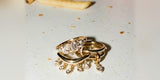 Gold rings with crystal dangles resting on a white table beside a scattered fry and crumbs