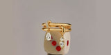 A gold Oomiay ring with crystal drops balanced on a stack of dice