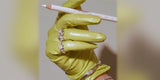 A chartreuse leather glove holding a white pencil, with crystal rings and a bangle worn over the glove