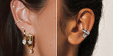 A gold ear stack with huggies and dangles beside a silver heart ear cuff