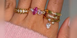 A hand wearing Oomiay gold rings on several fingers against a pink sweater