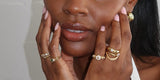 Hands framing a face, wearing Oomiay gold rings on several fingers