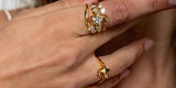 A hand at a woman's chin wearing a gold star ring stacked with small crystal rings, and a small star ring on the next finger