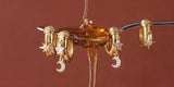 Gold charm huggie earrings with stars and moons hanging from a honey spoon