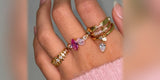 A hand in a pink sweater sleeve wearing stacked gold rings with pink, white and pear crystals