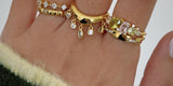 A hand in a green knit sleeve wearing stacked gold rings with crystal drops