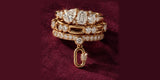 A stack of Oomiay gold rings with crystals and a charm on red velvet
