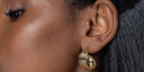 A woman wearing Oomiay Koi earrings, sculpted gold hoops on stainless steel posts