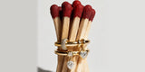 Two gold Oomiay rings with dangle charms stacked around a bundle of red-tipped matchsticks